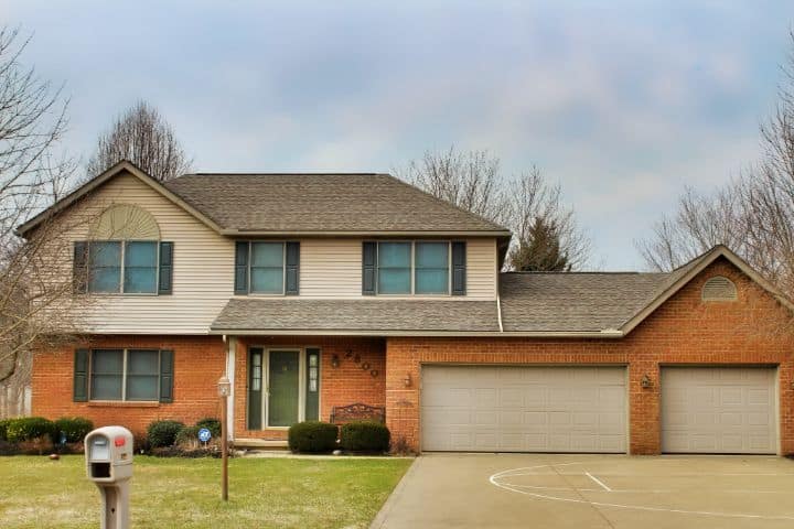 beige siding on home with brown shingled roof done by roofers near me and brick siding on the first level and three car garage