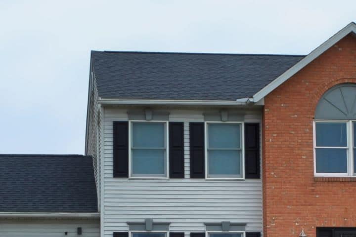 zoomed in view of upstairs of home with new roofing companies shingle roof installation and siding contractors installation of new light gray siding