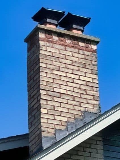 beige chimney with chimney cap and step flashing on the roof of house