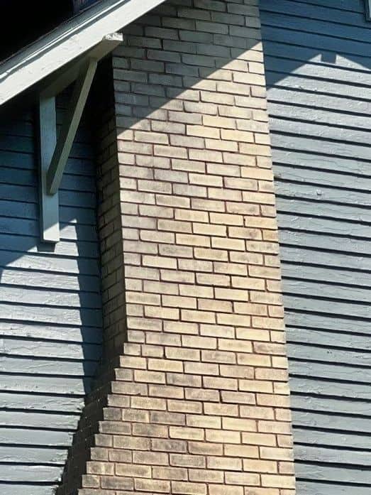 beige brick chimney rebuild by masonry contractors in Mansfield Ohio with blue siding on each side of the chimney