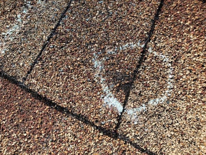 overhead closeup view of brown shingled roof with a circle chalk mark identifying what does hail damage look like