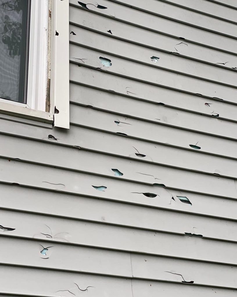 sideview of gray vinyl siding with lots of cracks and holes to show what does hail damage on siding look like