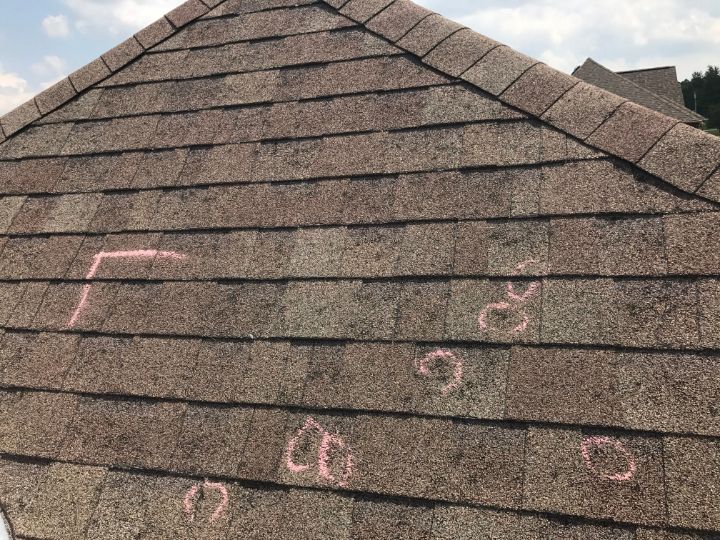 sideview of the peak of a brown shingled roof with pink chalk markings signifying what does hail damage look like